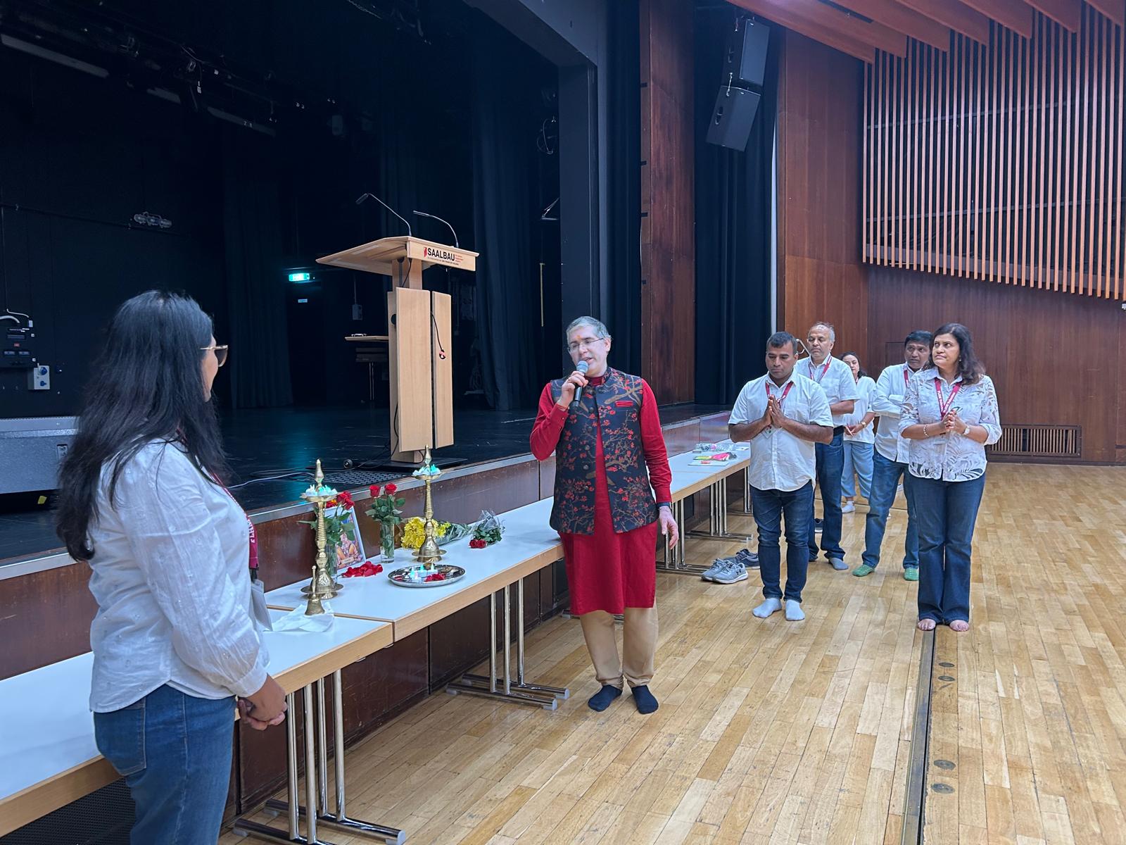 Organizer addressing attendees on stage with traditional diya and floral decor at the HMEurope Frankfurt event